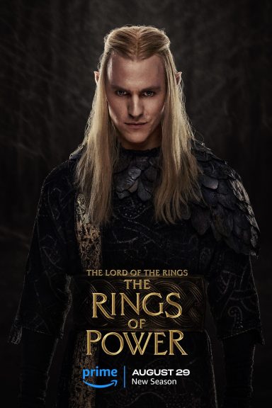 Rings of Power Season 3 A character with long blond hair, wearing dark, ornate attire, set against a shadowy background.